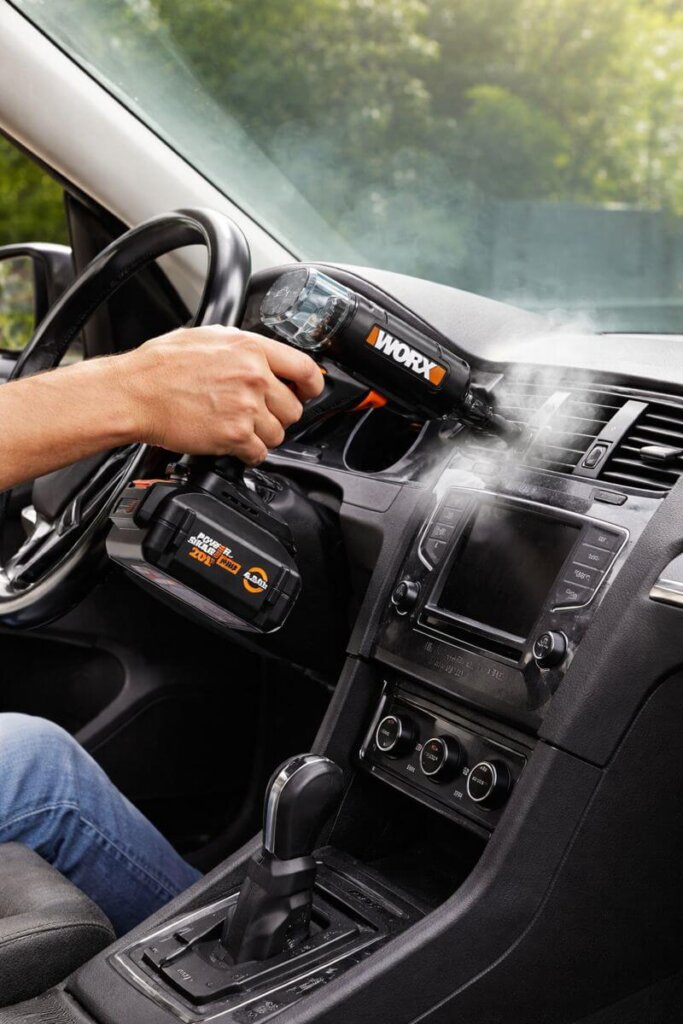 Worx 20V SteamStorm cordless steam cleaner detailing a car interior dashboard and air vents using high-pressure steam